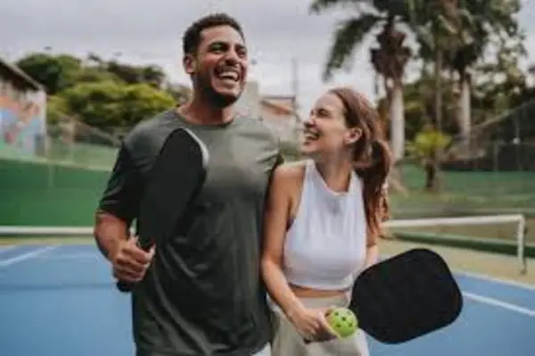Pickleball Image A man and woman stand together on a blue tennis court, each holding a paddle, smiling in a casual, outdoor setting.
