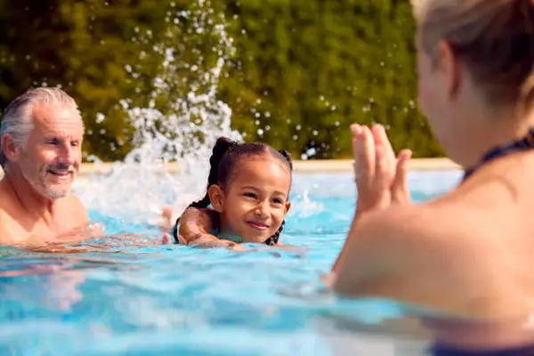 Pool Stock Image A child is swimming in a pool, splashing water, while an adult engages and encourages from the side. Bright, sunny day, lush greenery in background.